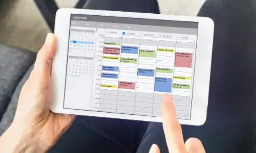 Hands using tablet to view and manage digital calendar schedule.