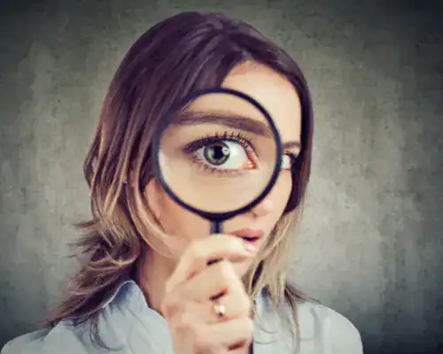 Woman looking intently through a magnifying glass, eye magnified.
